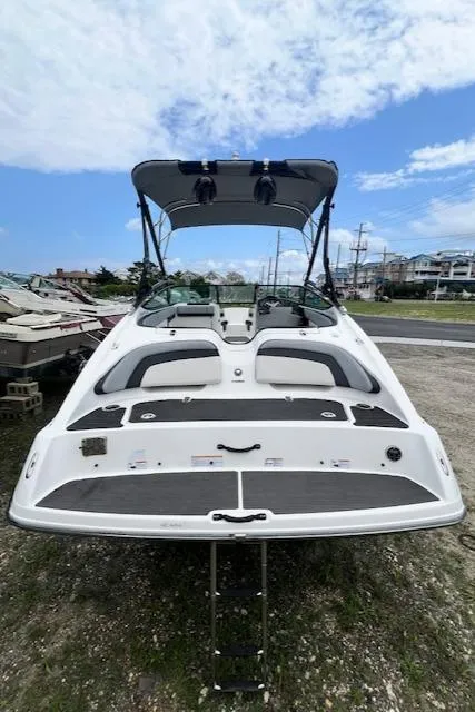 Slide: The Image of 2013 Yamaha Boats 212X with wakeboard tower, parked on gravel, under a partly cloudy sky. - 2