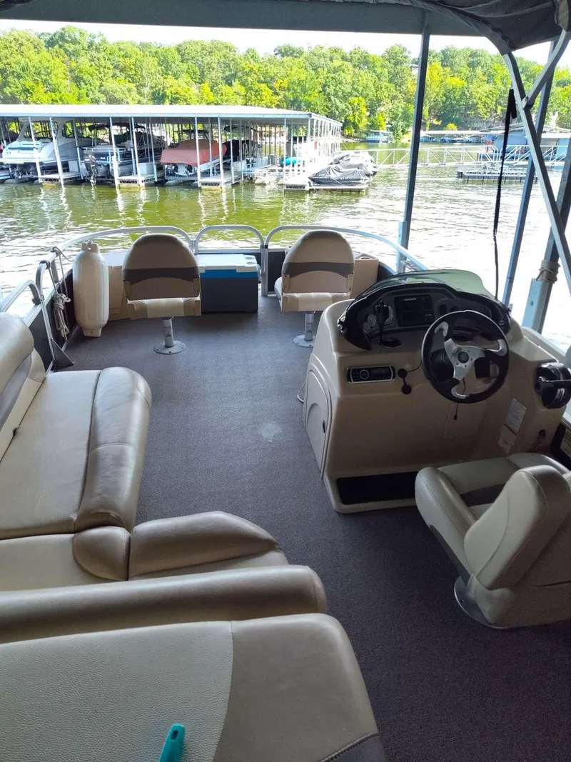 Slide: The Image of 2016 Sun Tracker Fishin' Barge 22 DLX interior with seating and steering, docked by a marina. - 4
