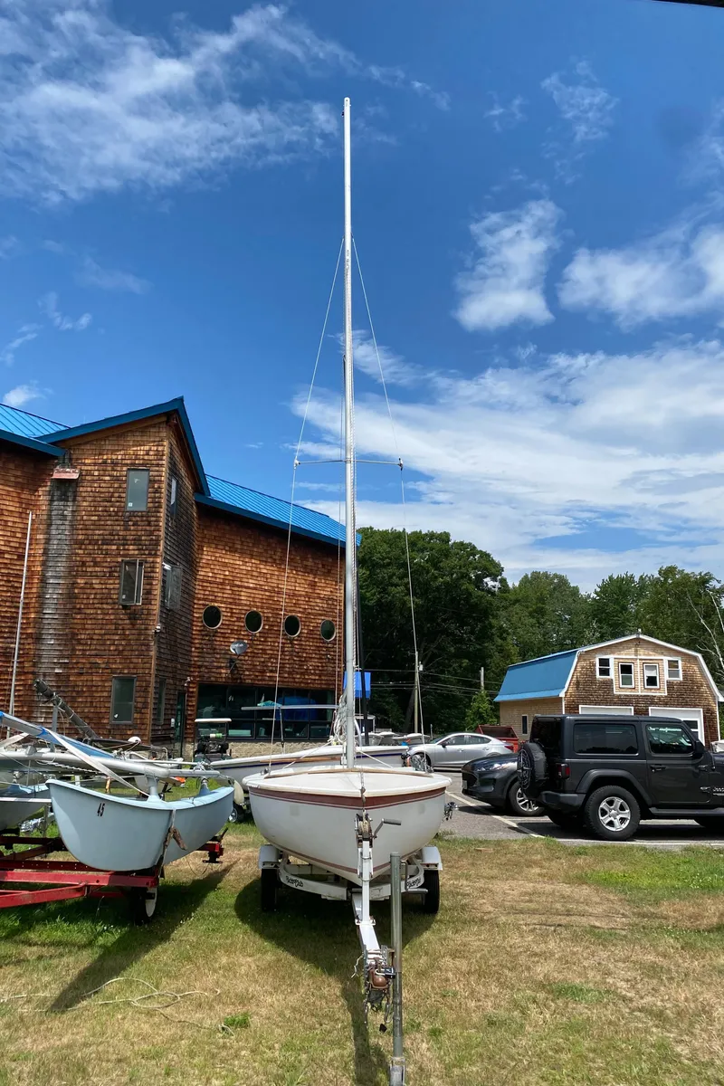 Slide: The Image of Catalina CAPRI 14.2 sailboat on trailer, parked near rustic buildings, under a clear blue sky. - 4
