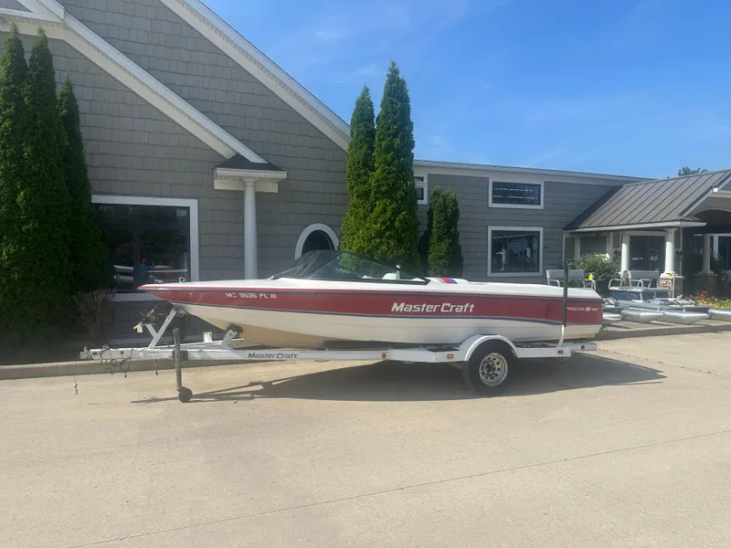 The Image of 1993 MasterCraft ProStar 190 boat on trailer, parked outside a building on a sunny day. - 0