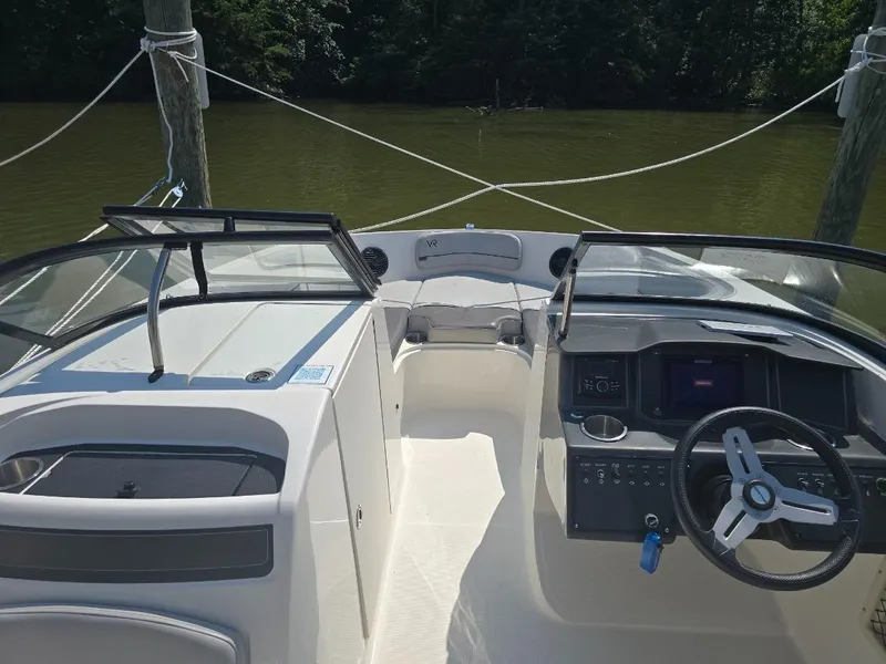 Slide: The Image of 2022 Bayliner VR6 Bowrider OB interior with steering wheel and seating, docked on calm water. - 5