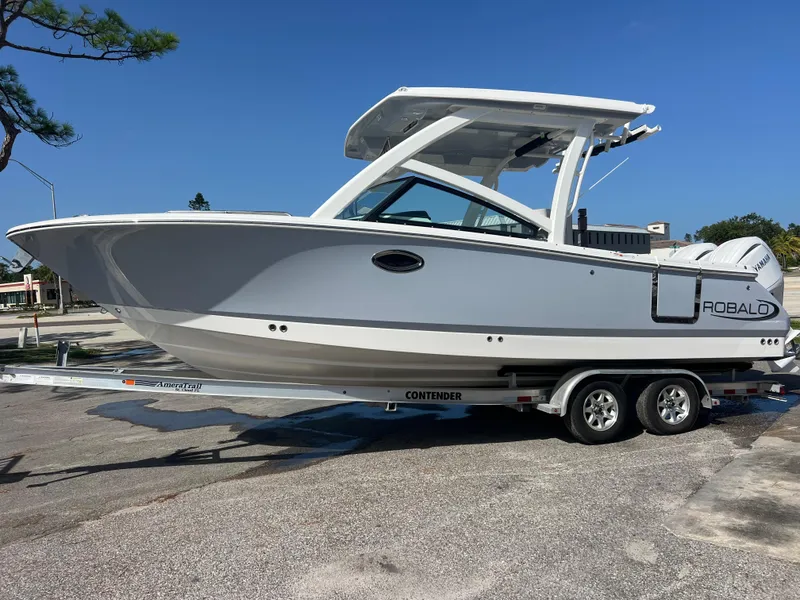Slide: The Image of 2025 Robalo R257 Dual Console boat on trailer, parked outdoors under clear blue sky. - 2