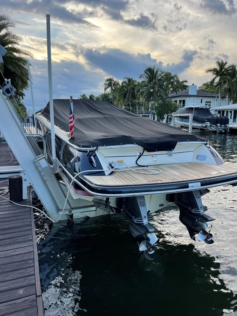 Slide: The Image of 2015 Chris-Craft 32 Launch boat docked with cover, surrounded by palm trees and waterfront homes. - 33