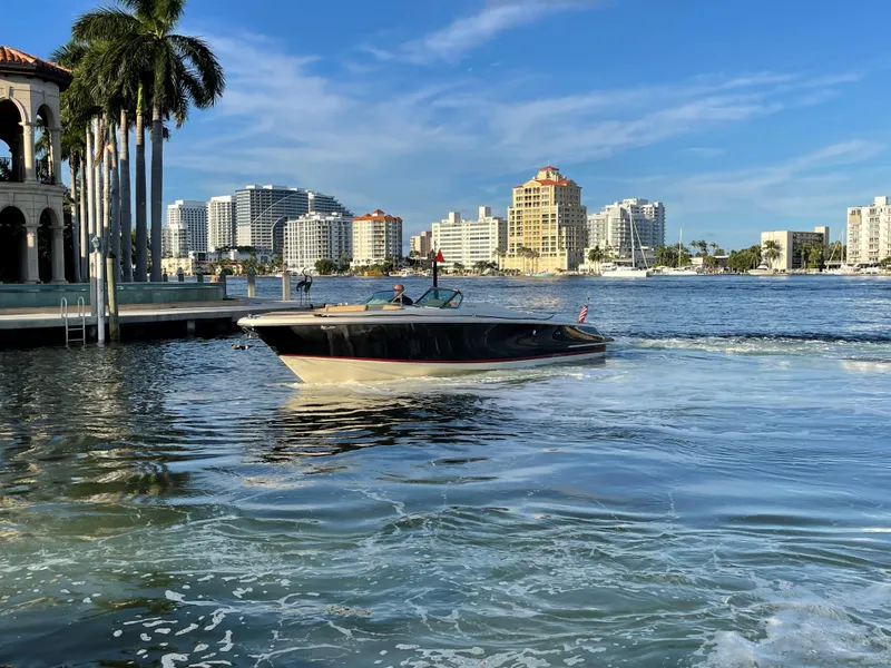 Slide: The Image of 2015 Chris-Craft 32 Launch boat cruising near a city waterfront with palm trees. - 5