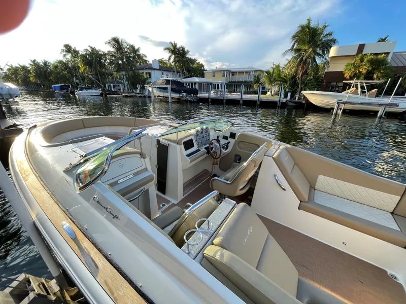 Slide: The Image of 2015 Chris-Craft 32 Launch boat docked by waterfront homes, featuring luxurious seating and controls. - 8