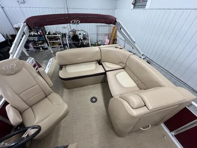 Slide: The Image of 2016 Harris Solstice 220 SL pontoon boat with beige seating and maroon canopy in a garage. - 12
