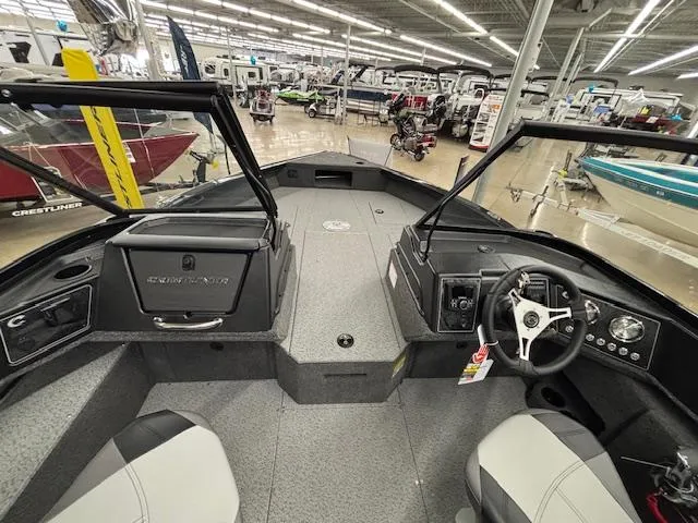 Slide: The Image of 2025 Crestliner 2050 Fish Hawk boat interior, featuring steering wheel and seating in a showroom. - 18