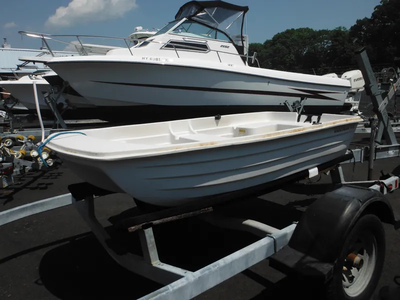 Slide: The Image of Sun Dolphin WATERTENDER 9.4 boat on trailer, parked near larger boat, sunny day. - 3