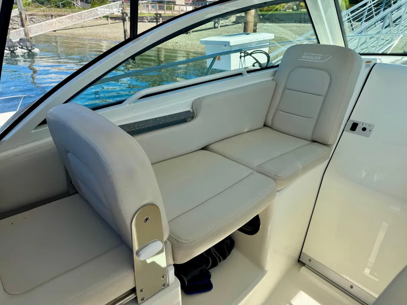 Slide: The Image of 2018 Boston Whaler 285 Conquest interior seating with beige upholstery, dockside view. - 11