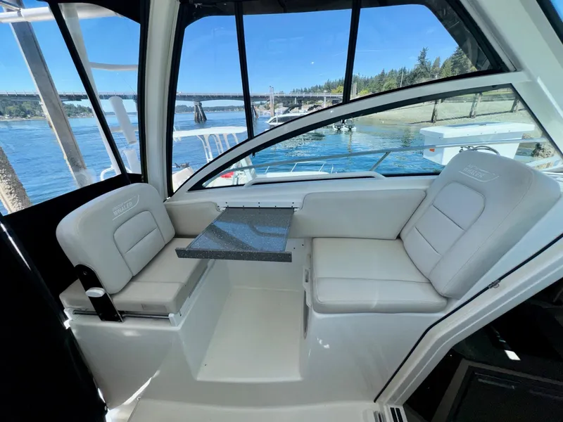 Slide: The Image of 2018 Boston Whaler 285 Conquest interior with seating and table, overlooking scenic waterfront. - 13