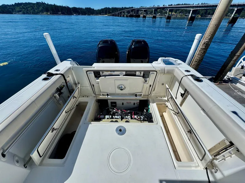 Slide: The Image of 2018 Boston Whaler 285 Conquest boat interior with open storage compartments, docked by a scenic bridge. - 3