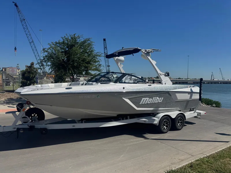 Slide: The Image of 2022 Malibu Wakesetter 24 MXZ boat on trailer by waterfront, clear sky background. - 25