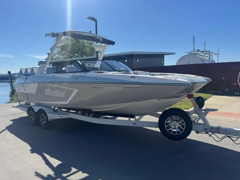 Slide: The Image of 2022 Malibu Wakesetter 24 MXZ boat on trailer, parked near waterfront under clear blue sky. - 26