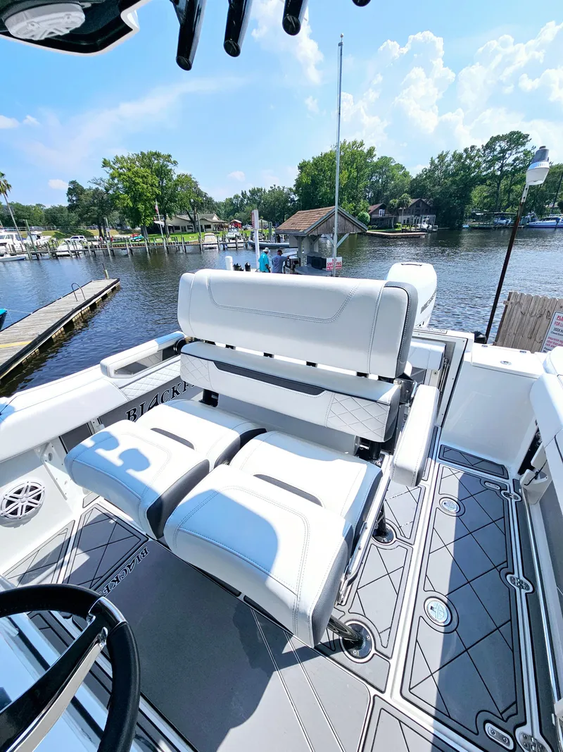 Slide: The Image of 2021 Blackfin 252 CC boat interior with white seating, docked by a scenic waterfront. - 15
