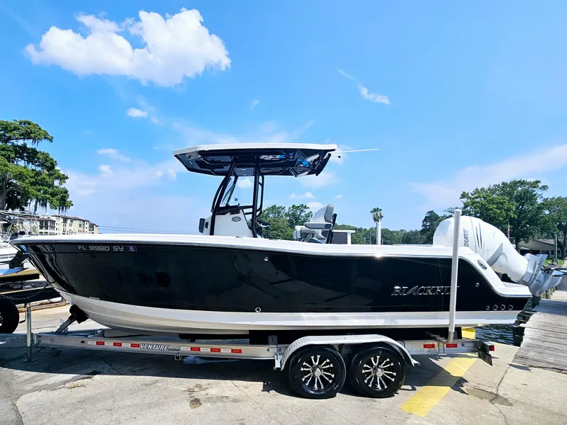 Slide: The Image of 2021 Blackfin 252 CC boat on trailer, parked outdoors under a clear blue sky. - 2