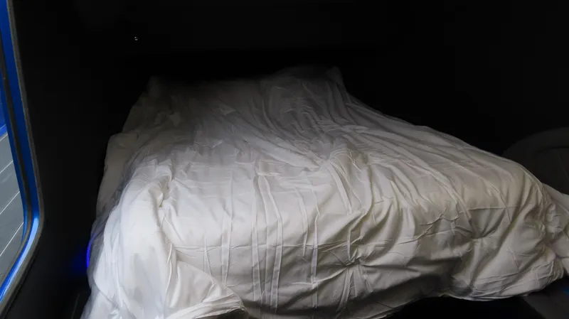 Slide: The Image of Cozy bed inside MTI 42V 2025 model, featuring white bedding and dim lighting. - 19