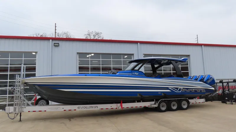 Slide: The Image of 2025 MTI 42V boat with blue and white design on a trailer outside a building. - 2