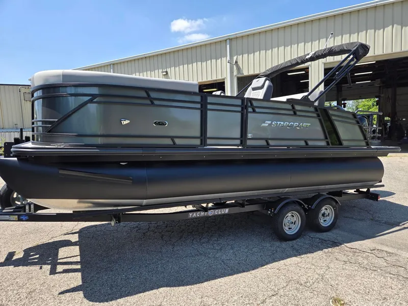 Slide: The Image of 2026 Starcraft EXS1QDH pontoon boat on trailer, parked outside a warehouse. - 4