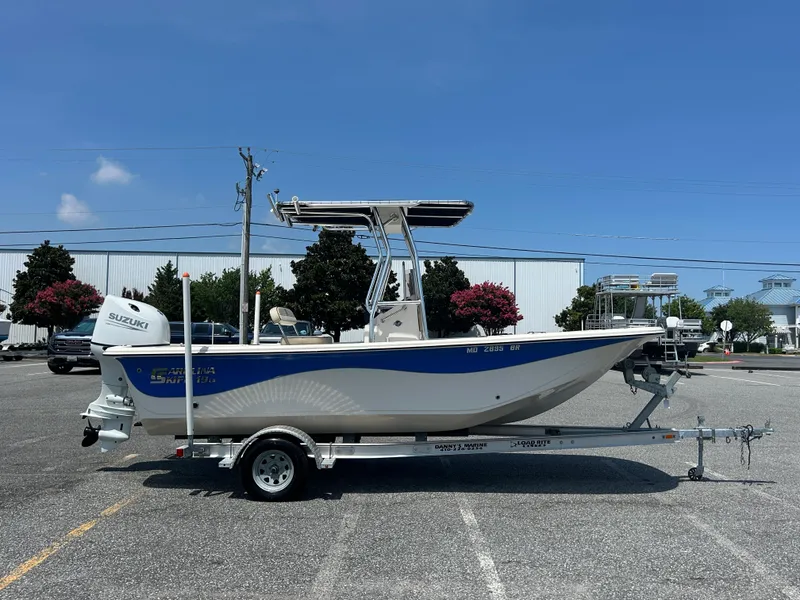Slide: The Image of 2022 Carolina Skiff 19 LS boat on trailer, parked outdoors under clear blue sky. - 6