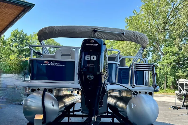 Slide: The Image of 2025 Sun Tracker Bass Buggy 18 DLX pontoon boat with Mercury 60 engine, parked outdoors. - 91