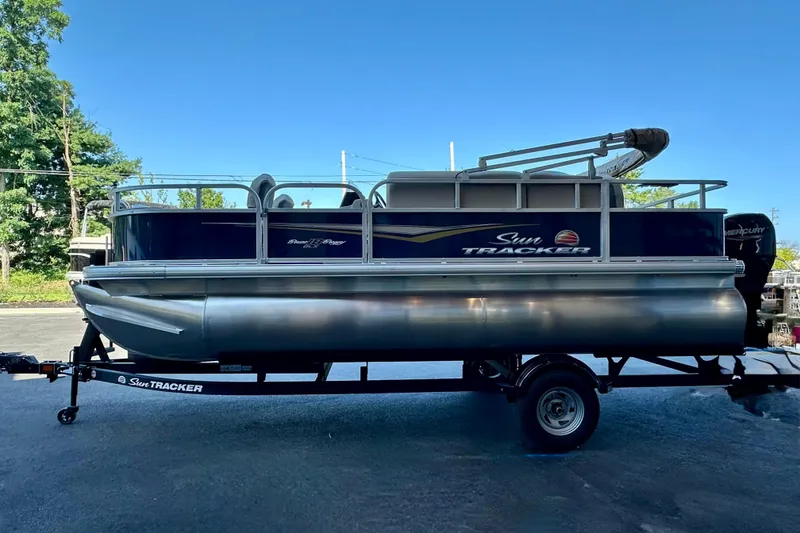 Slide: The Image of 2025 Sun Tracker Bass Buggy 18 DLX pontoon boat on trailer, parked outdoors. - 92