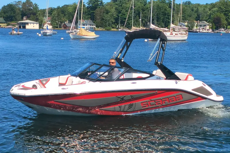 Slide: The Image of 2023 Scarab 195 ID boat cruising on a scenic lake with sailboats in the background. - 0