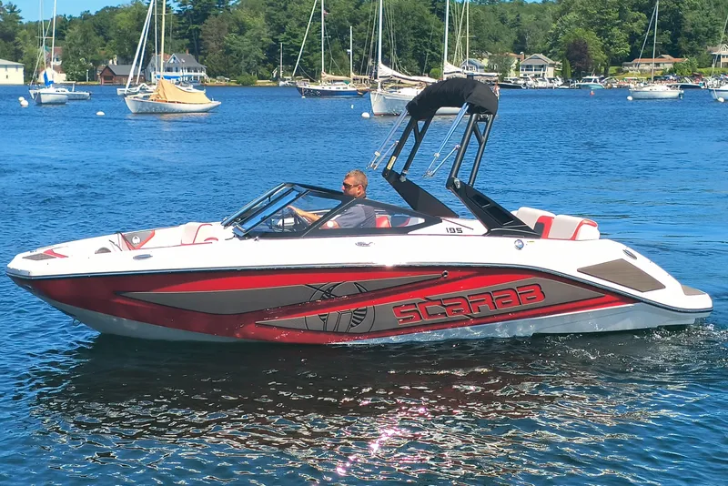 Slide: The Image of 2023 Scarab 195 ID boat cruising on a scenic lake with sailboats in the background. - 1