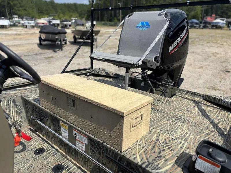 Slide: The Image of 2025 Tracker GRIZZLY® 1860 CC boat with Mercury engine and storage box, parked outdoors. - 11