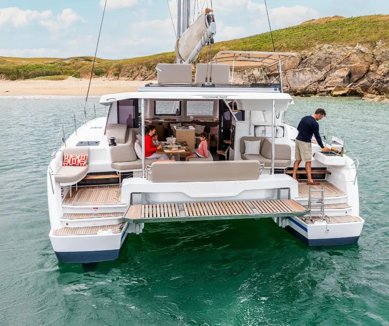 Slide: The Image of 2025 Fountaine Pajot NEW 41 catamaran with people dining onboard, anchored near a beach. - 42