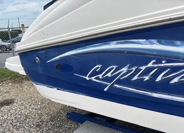 Slide: The Image of 2006 Rinker 232 Captiva Bowrider boat, blue and white exterior, parked on gravel. - 27