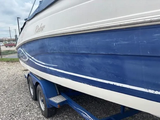 Slide: The Image of 2006 Rinker 232 Captiva Bowrider on trailer, blue and white exterior, parked on gravel. - 29
