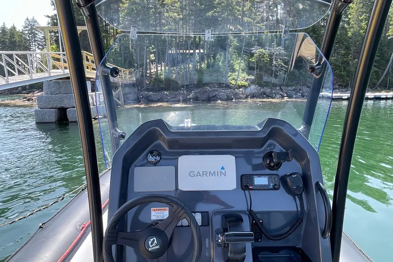 Slide: The Image of 2022 Zodiac Open 7 boat dashboard with Garmin navigation, docked near a forested shoreline. - 32