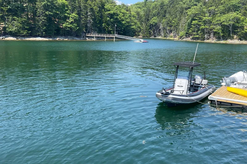 Slide: The Image of Zodiac Open 7 boat docked on a serene lake with lush forest background. - 7