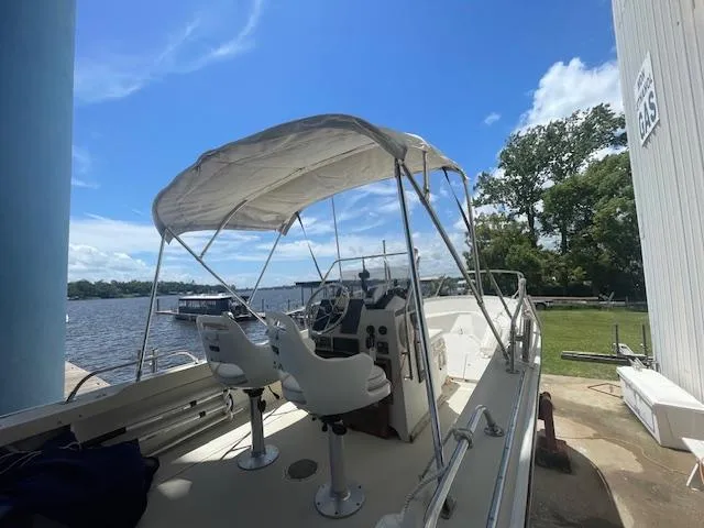 Slide: The Image of 1989 Boston Whaler 21 Outrage boat with canopy, docked by a scenic riverside. - 2