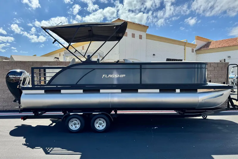 The Image of 2025 Flagship E22RF pontoon boat with Mercury engine, parked on a trailer under a sunny sky. - 0