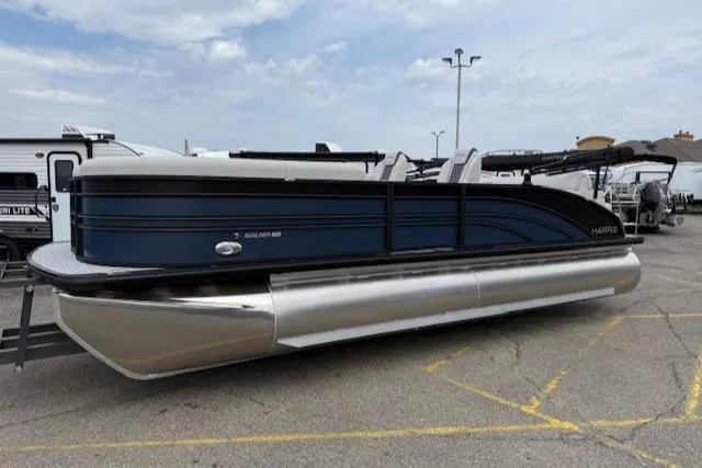 Slide: The Image of 2025 Harris Sunliner 230 pontoon boat parked in a lot under a cloudy sky. - 2