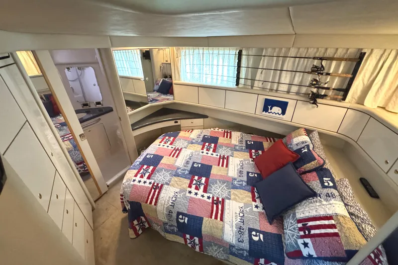 Slide: The Image of 1997 Sea Ray 370 Aft Cabin bedroom with colorful quilt, pillows, and fishing rods. - 22