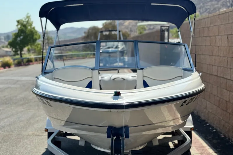 Slide: The Image of 2004 Bayliner 175 Bowrider boat with blue canopy on a trailer, parked outdoors. - 2