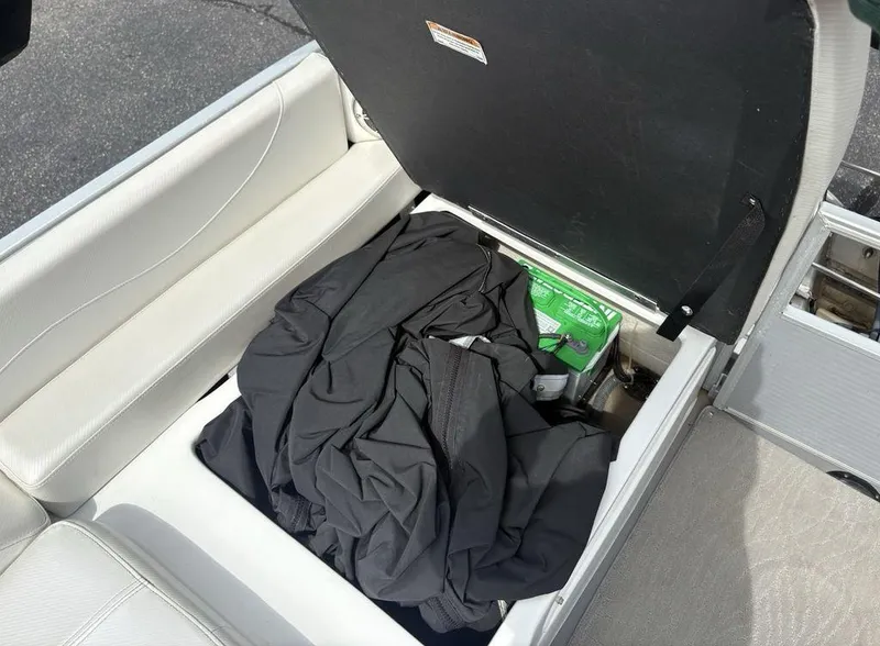 Slide: The Image of Open storage compartment in 2013 Godfrey AP250 RL boat with black cover and green battery. - 28