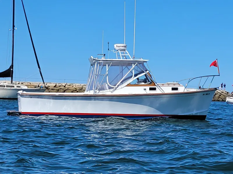 Slide: The Image of 1993 Fortier 26 boat on water, clear sky, docked sailboats in background. - 4
