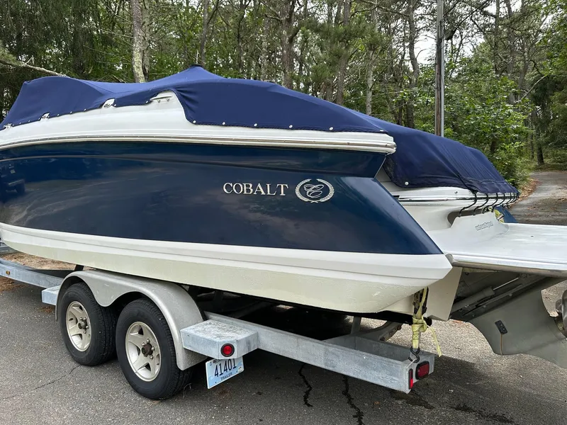 Slide: The Image of 2010 Cobalt 262 boat on trailer with blue cover, parked in wooded area. - 3