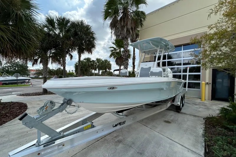 Slide: The Image of 2025 Mako 24 APEX boat on trailer, parked outdoors near palm trees. - 2