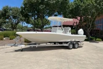 The Image of 2025 Ranger 2510 Bay boat on trailer, parked outdoors near trees and building. - 0