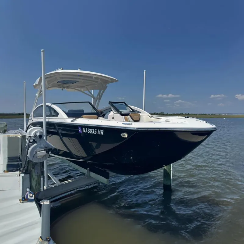 The Image of 2022 Yamaha Boats 275SD on lift, docked by calm waters under clear blue sky. - 0