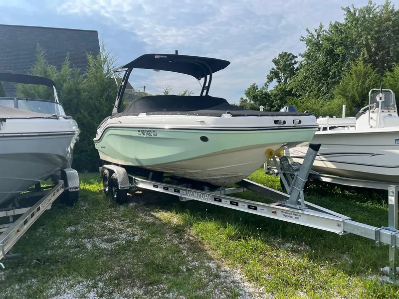 Slide: The Image of 2023 Bayliner DX 2000 boat on trailer, parked outdoors with other boats. - 2