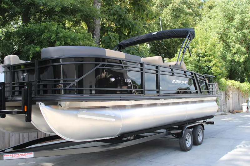 The Image of 2026 Starcraft CX 23 RL pontoon boat on trailer, surrounded by lush greenery. - 1