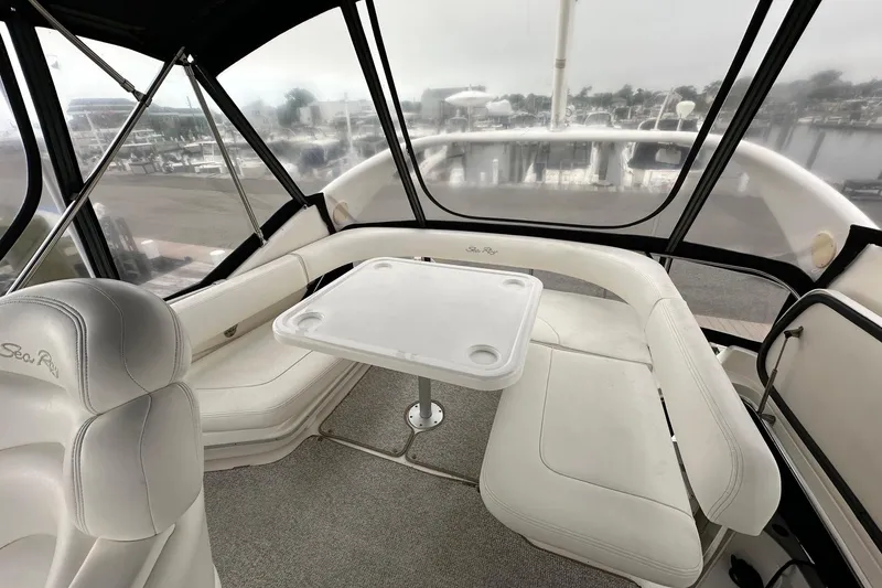 Slide: The Image of 2002 Sea Ray 400 Sedan Bridge interior with white seating and table, overlooking marina. - 18