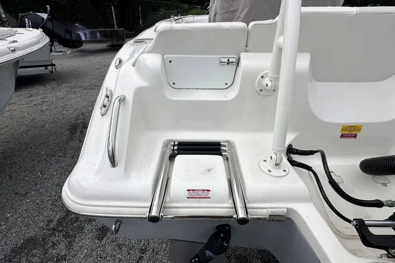 Slide: The Image of 2026 Key West 219 FS boat stern with ladder and railing, parked on gravel. - 6