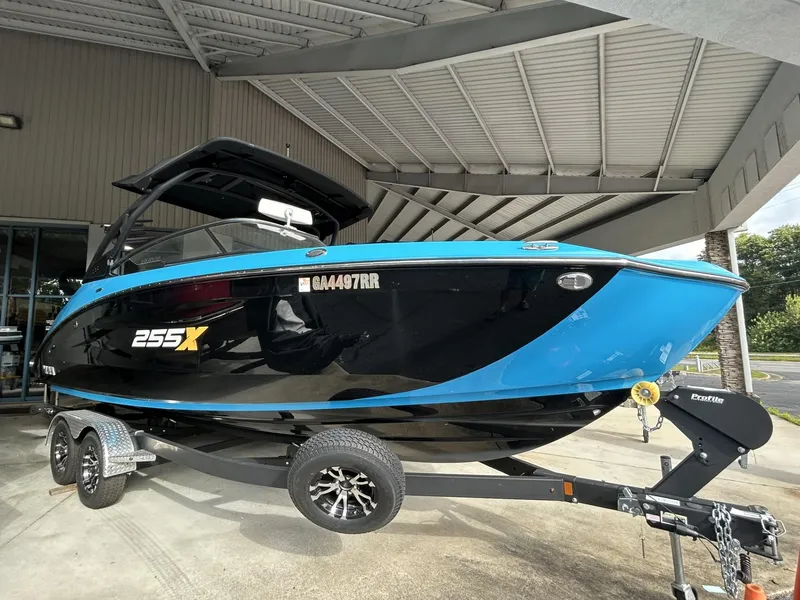 Slide: The Image of 2023 Yamaha Boats 255 XD in black and blue on trailer under a canopy. - 2