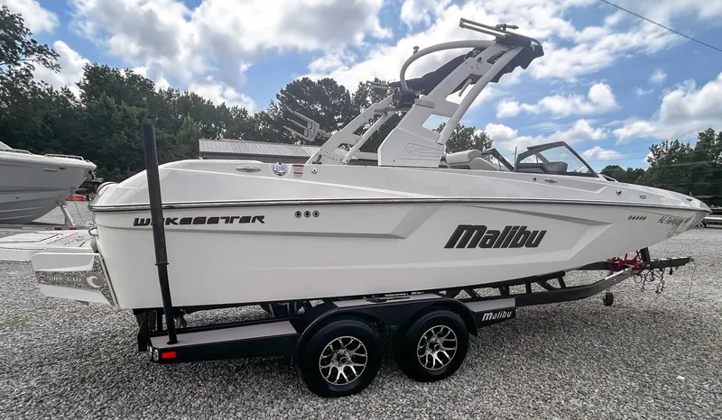 Slide: The Image of 2020 Malibu 23 MXZ boat on trailer, white exterior, parked on gravel lot. - 5